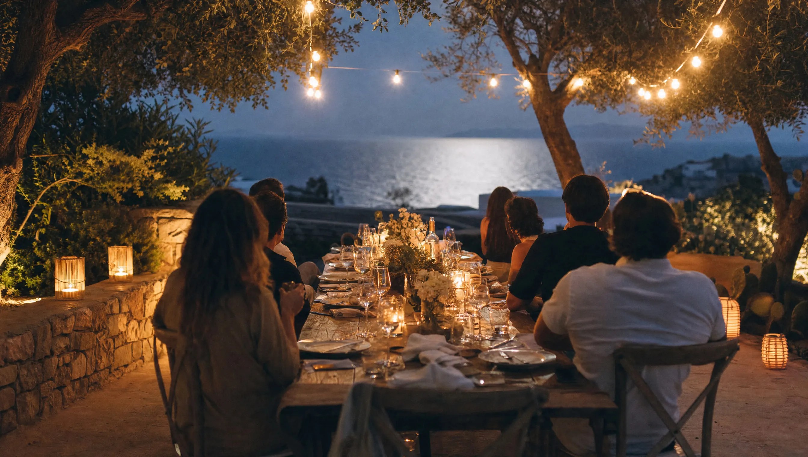 Lange Tafel bei einem gemeinsamen Abendessen unter Lichterketten am Abend